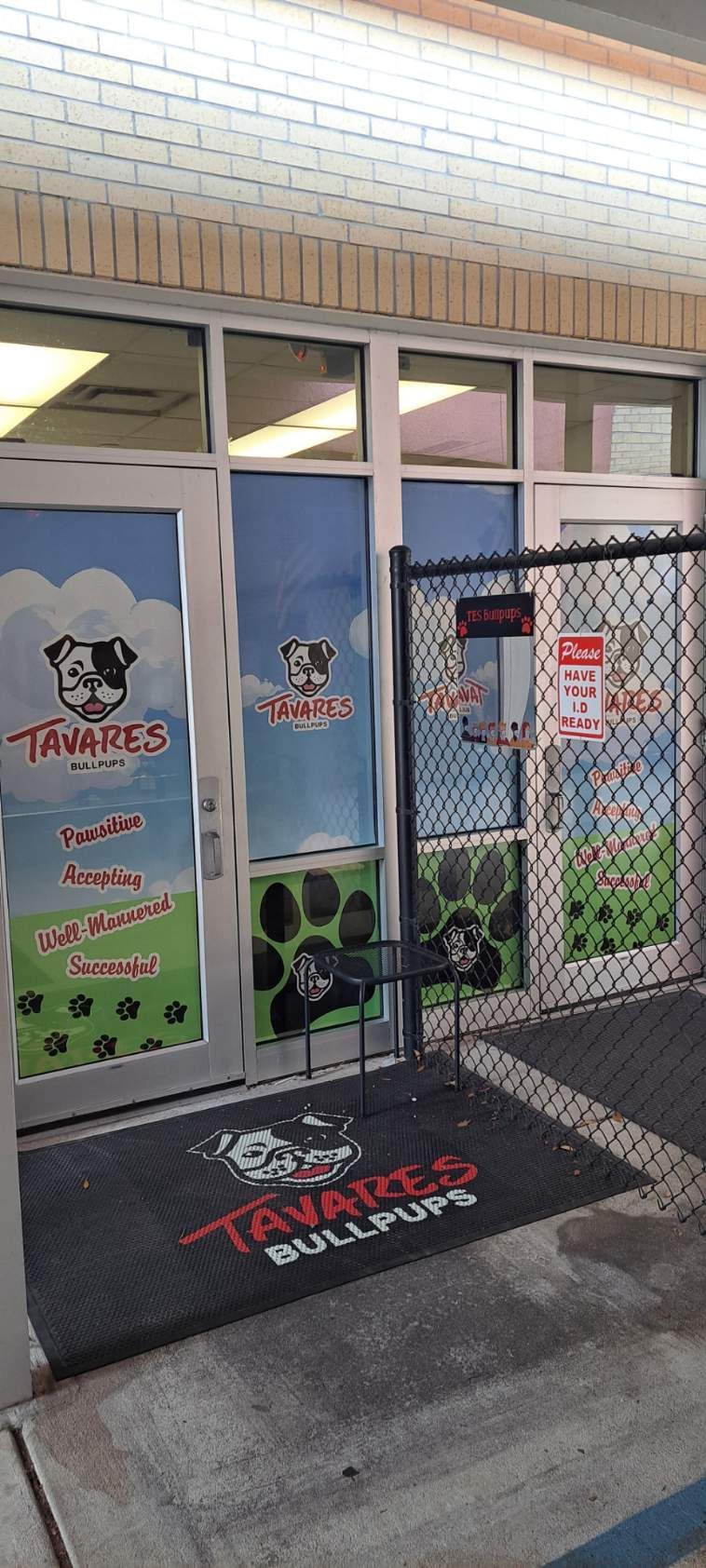 Exterior view of Tavares Bulldogs, a dog care facility, with a chain link fence and a welcome mat.
