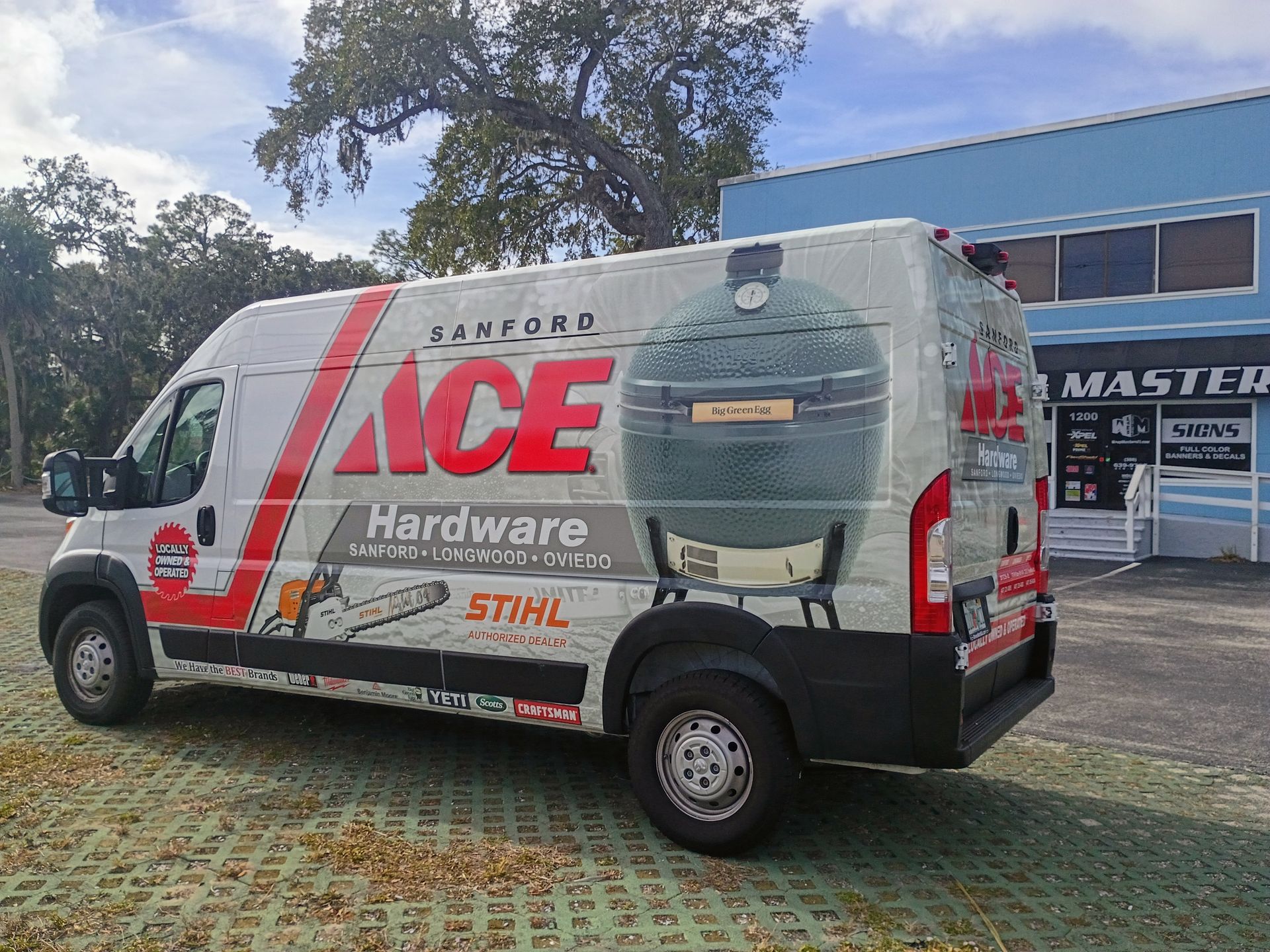 White Ace Hardware van with large grill graphic parked outside a store on a sunny day.