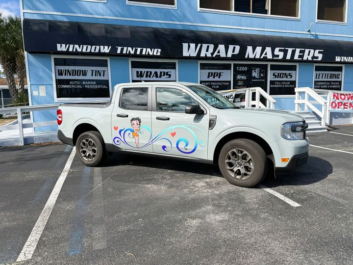 Gray pickup truck with graphic wrap parked outside "Wrap Masters" business.