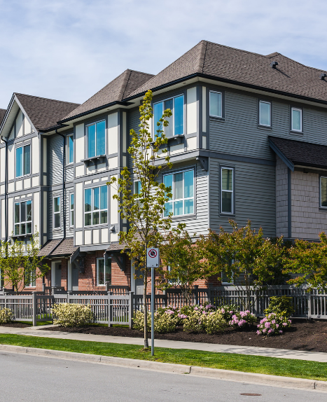Modern gray apartment buildings with blue window trim and landscaped front walk along a street