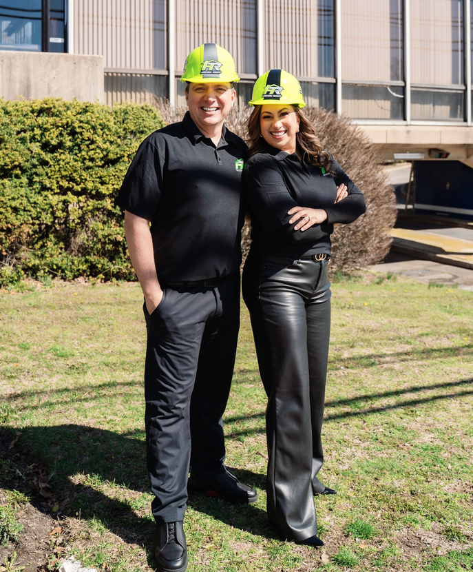 Two people in hard hats and black clothing standing outside the Hogan Roofing building.
