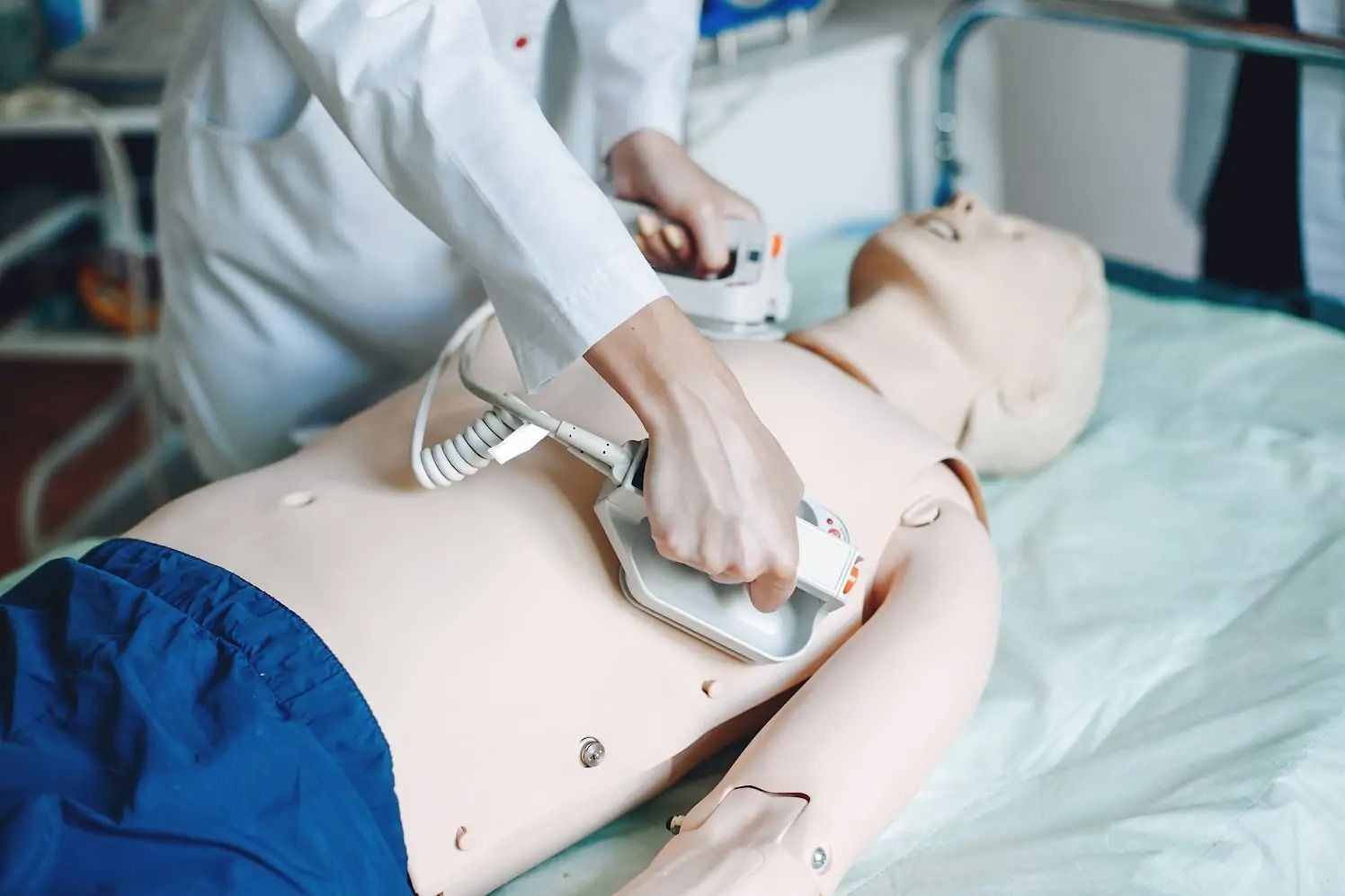 Person using a defibrillator on a mannequin in a hospital setting.