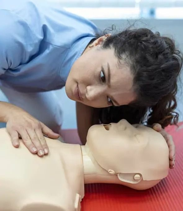 Woman performing CPR on a mannequin in a training setting.