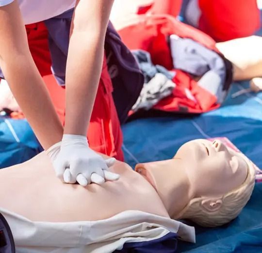 Person giving chest compressions on a CPR training dummy outdoors.