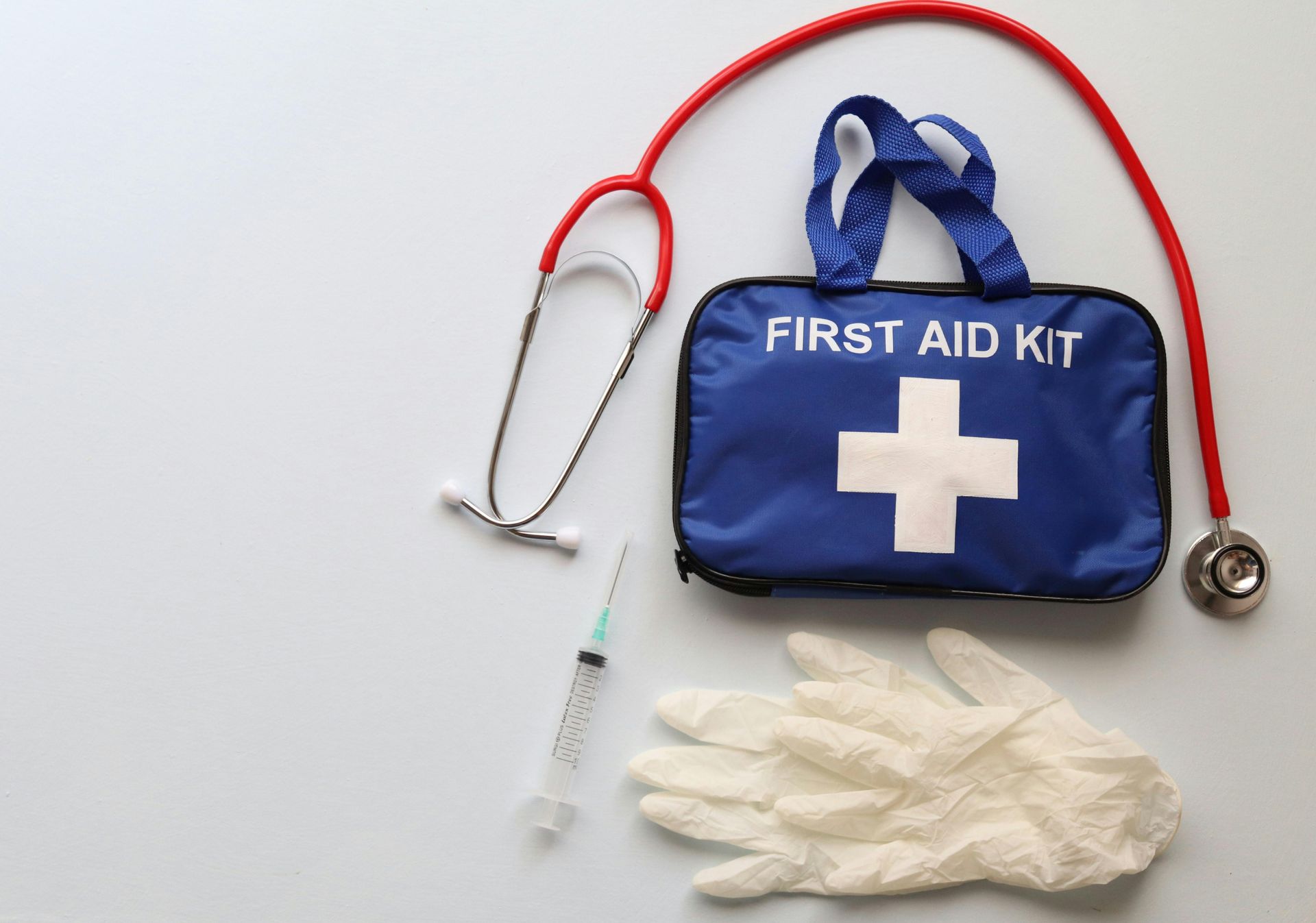 Blue first aid kit with white cross, stethoscope, syringe, and gloves on white background.