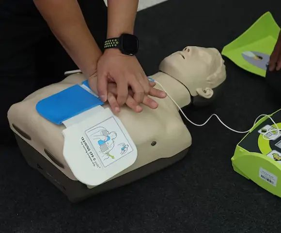 Person performing CPR on a mannequin, with AED pads attached.