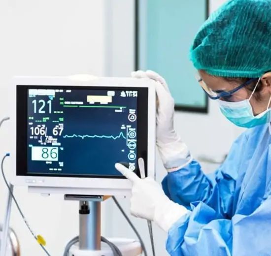 Doctor in surgical attire monitors vitals on a medical display screen with a blue background.