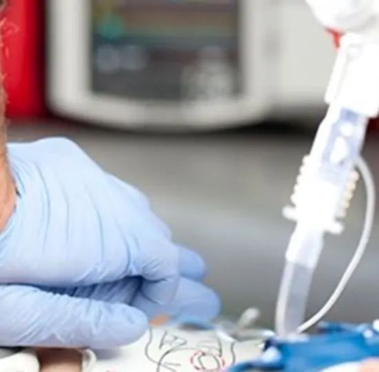 Gloved hand adjusting breathing tube on a patient; medical equipment in background.