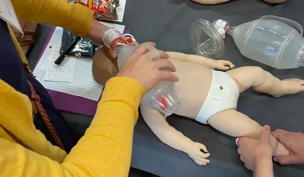 Person giving CPR to a baby-sized mannequin with an oxygen bag.