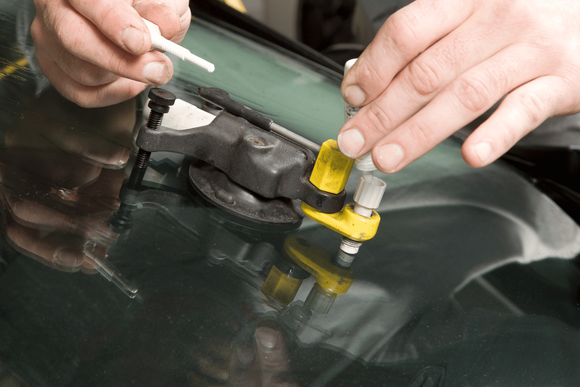 Hands applying a yellow suction tool to a cracked car windshield