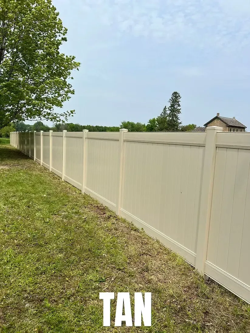 A tan vinyl privacy fence with lattice accents, stretching across a grassy lawn under a blue sky.