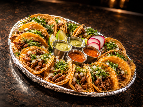 Four tacos filled with chopped meat, onions, cilantro, and salsa on a wooden board