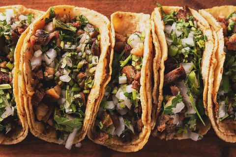 Four tacos filled with chopped meat, onions, cilantro, and salsa on a wooden board