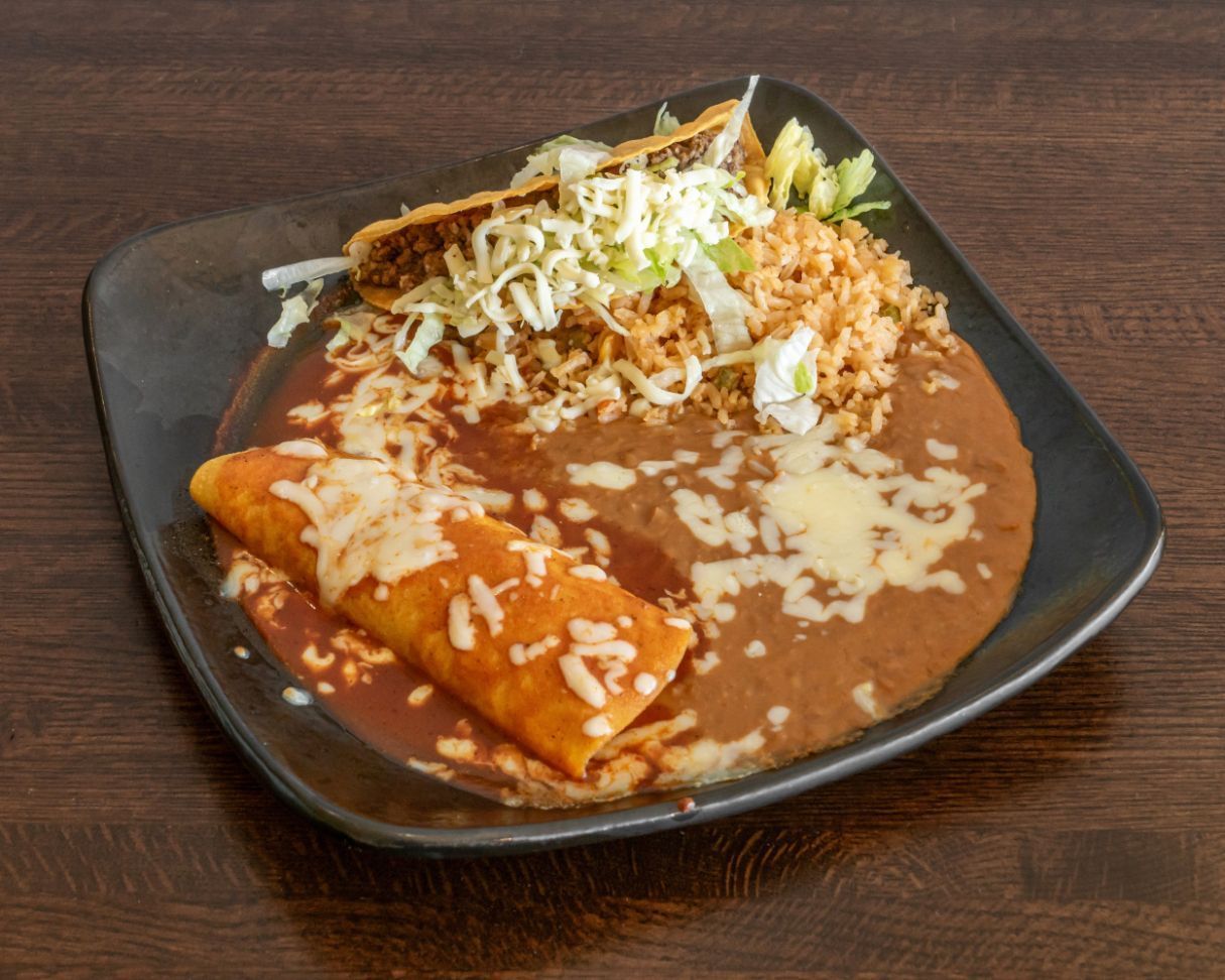 Plate of Mexican-style enchiladas with refried beans, rice, shredded cheese, and lettuce on a dark table