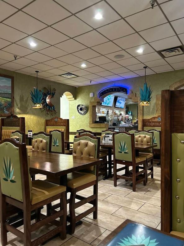 Empty restaurant dining area with wooden tables, green booths, and blue accent lighting near the back counter