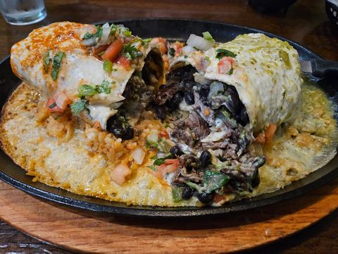 Stuffed enchiladas topped with green sauce and cheese on a plate, with rice and beans on the side