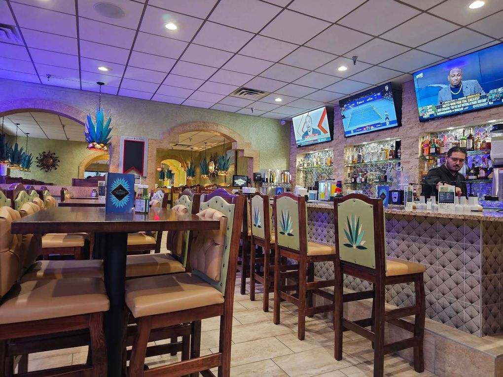 Empty restaurant bar with wooden tables, colorful ceiling lights, and TV screens above the counter