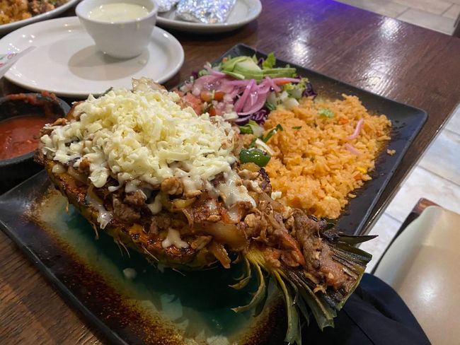 Grilled fish topped with cheese, served with rice, salad, and soup on a black plate