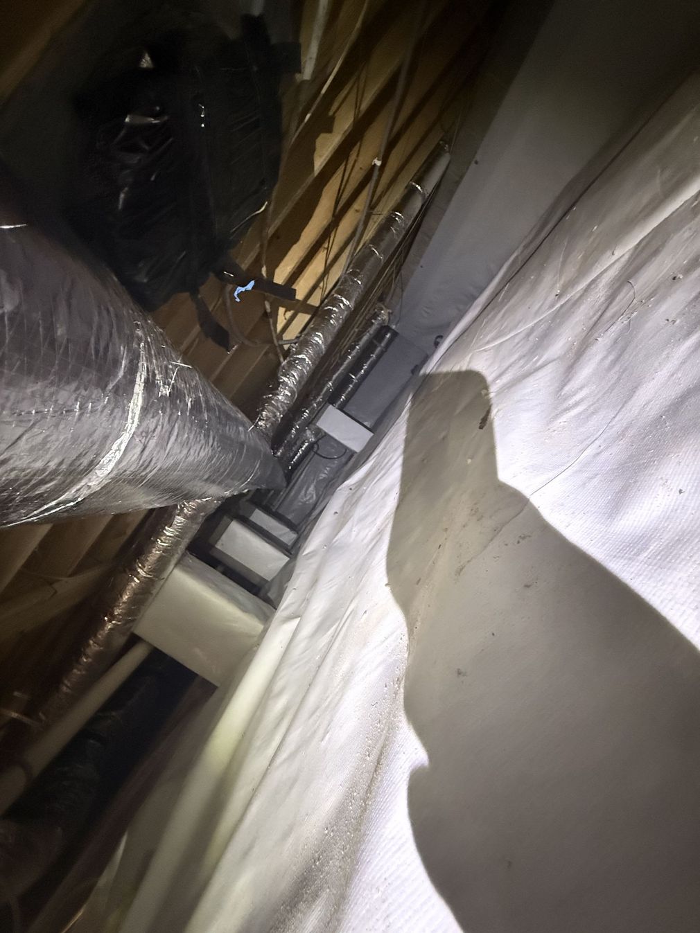 Inside a narrow attic crawlspace with insulation, beams, and a central pipe.