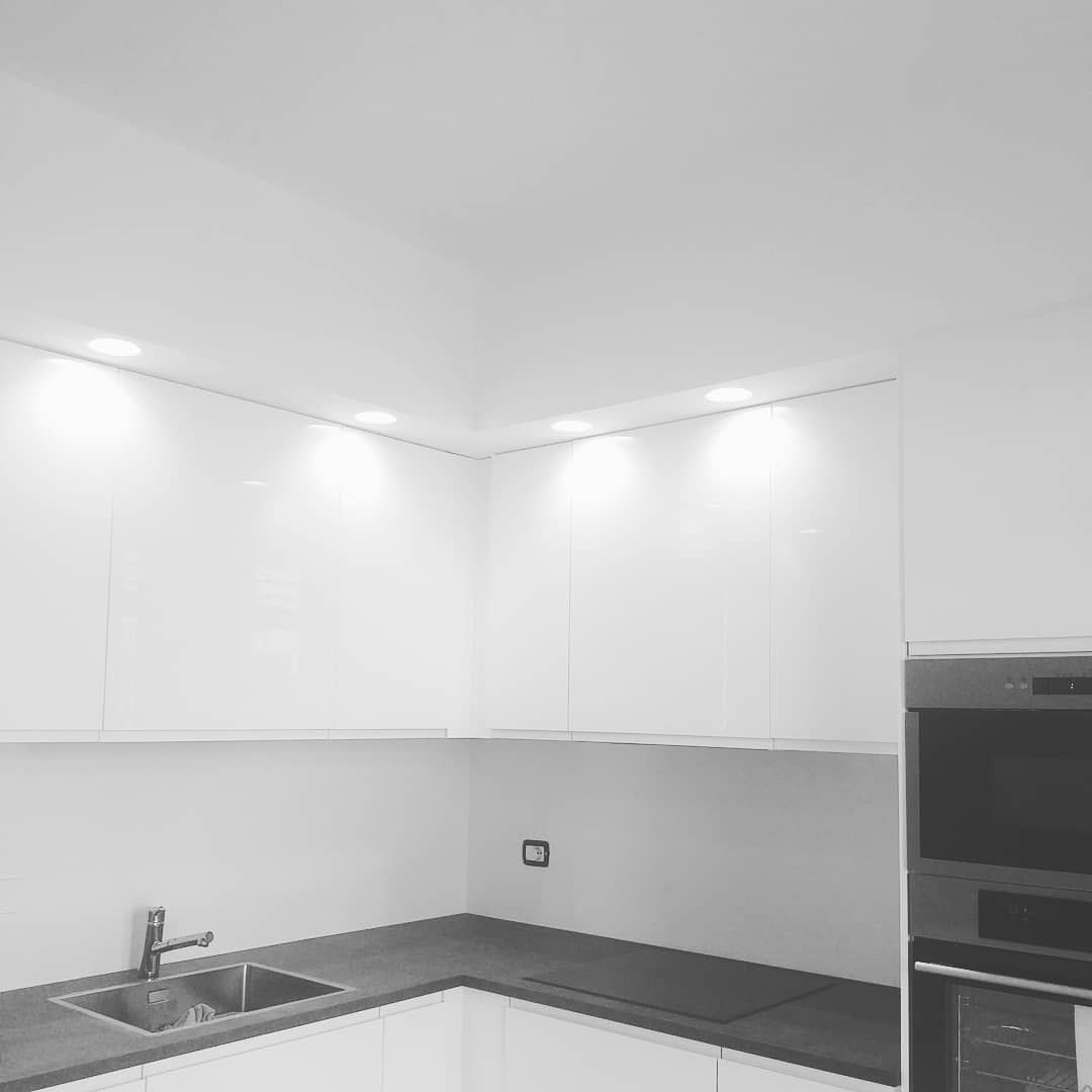 Angolo cottura moderno bianco con illuminazione dall'alto, lavello e forno incorporato.