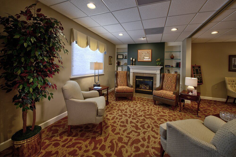 Cozy living room with fireplace, patterned carpet, chairs, and large window in a care-home lounge