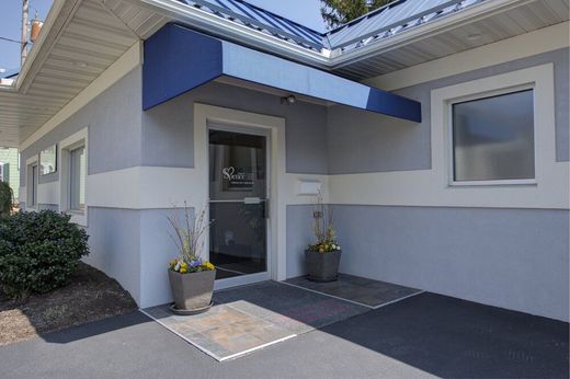 Building entrance with blue awning, glass door, and potted plants beside a paved walkway