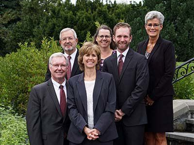Six people posing outdoors on steps in formal attire, with trees in the background.