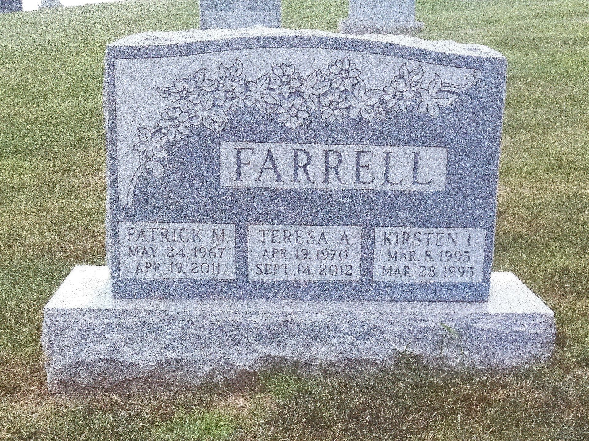 Farrell family gravestone in a grassy cemetery, with three smaller memorial plaques at the base
