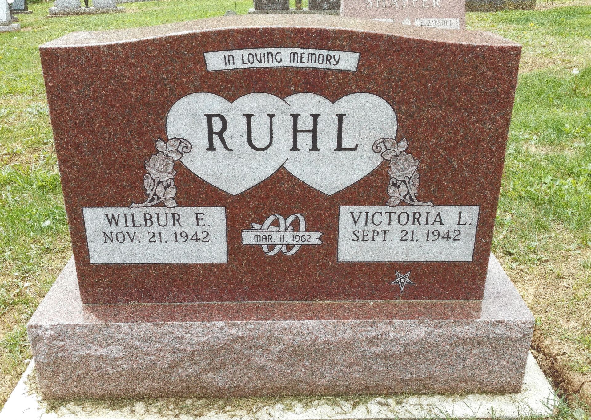 Brown granite gravestone engraved “RUHL” with two heart shapes and names Wilbur and Victoria