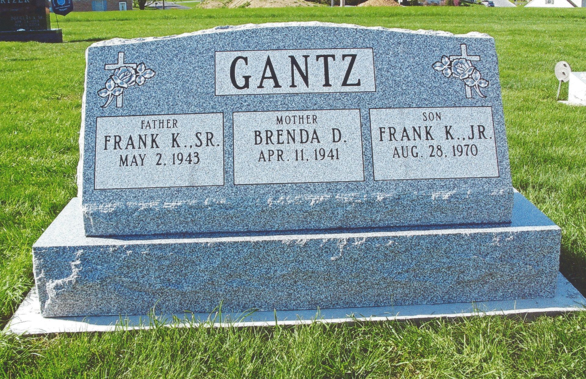 Blue granite family gravestone with three inset plaques in a grassy cemetery.
