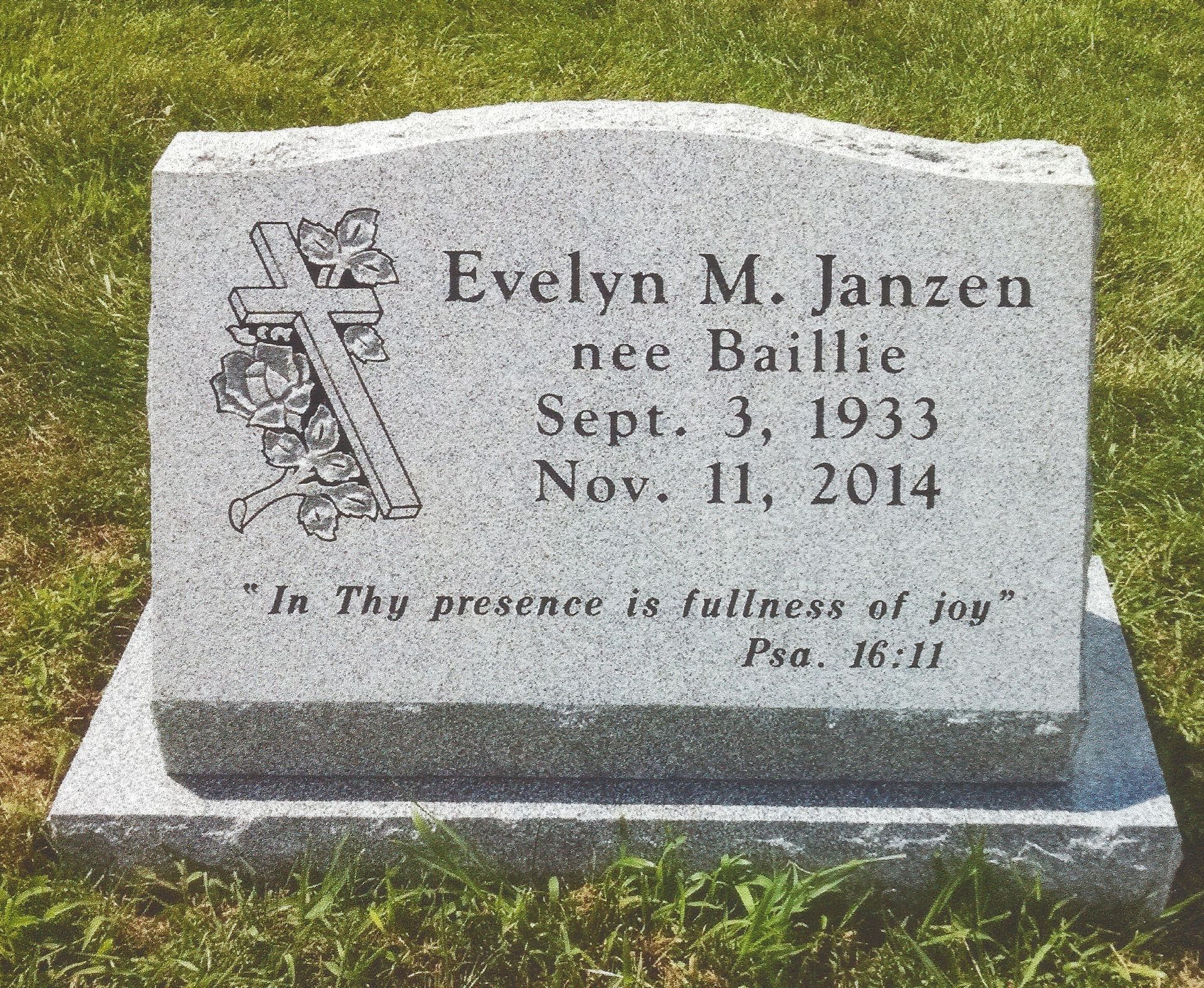 Gray gravestone with engraved name Evelyn M. Janzen, dates, and a Bible verse in a grassy cemetery.