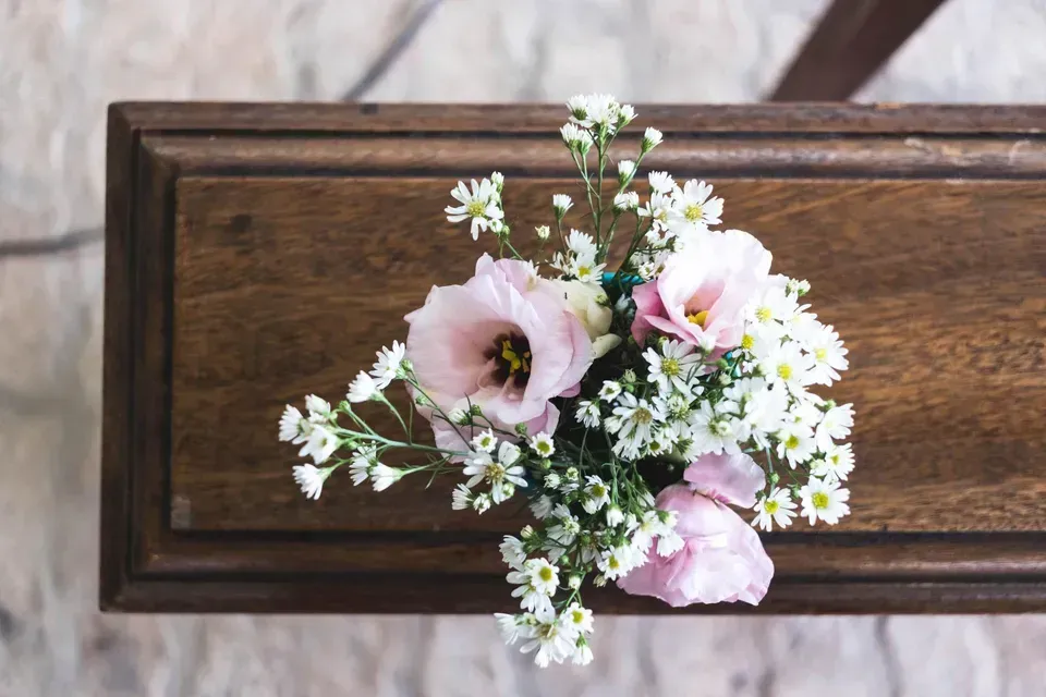 Pink and white flowers arranged in a small bouquet on a dark wooden casket