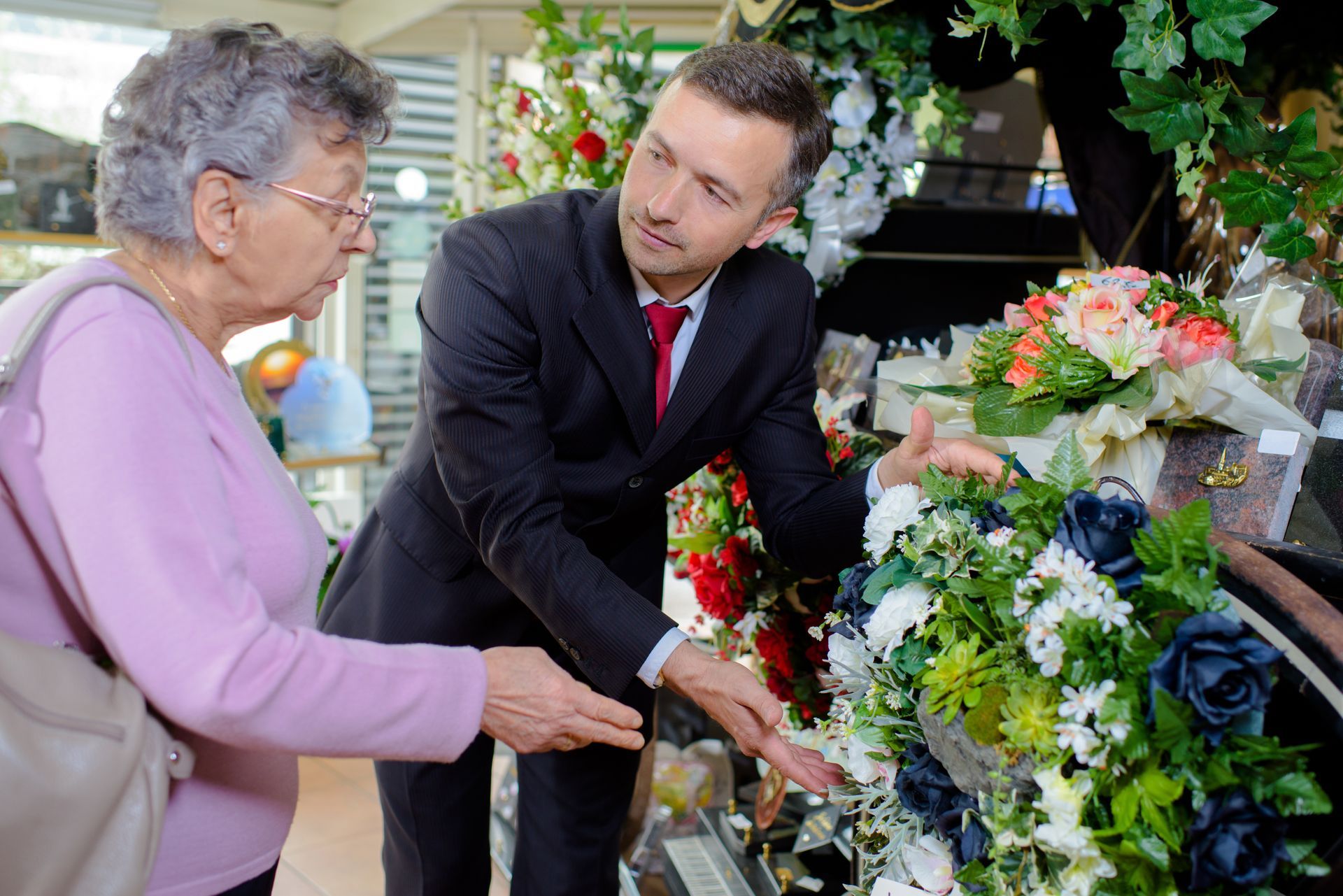 Two people examine flowers in a shop, with bouquets and floral arrangements on display.