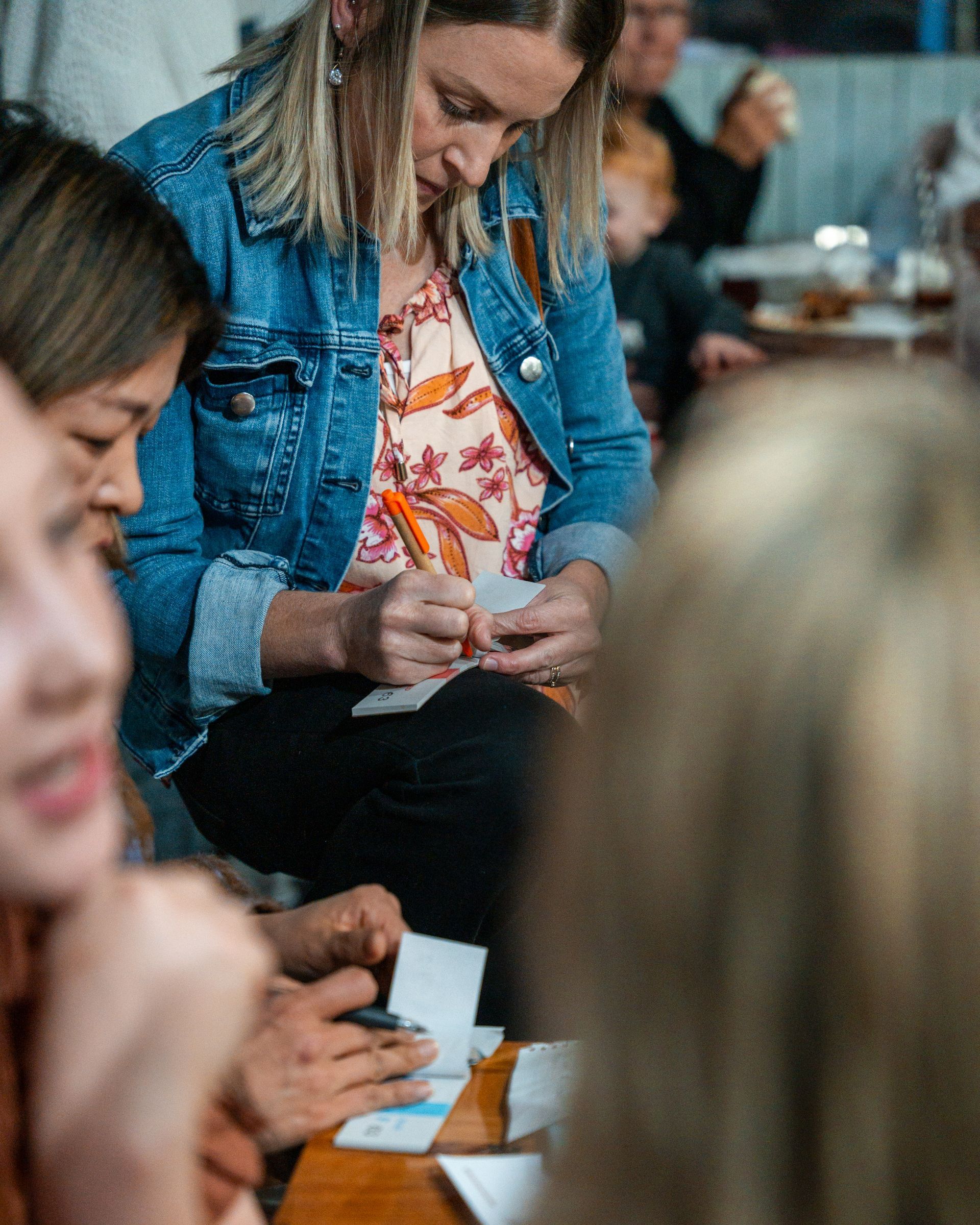 A Woman in A Denim Jacket Is Sitting at A Table Writing on A Piece of Paper — Chop 'n Chill in Port Macquarie, NSW