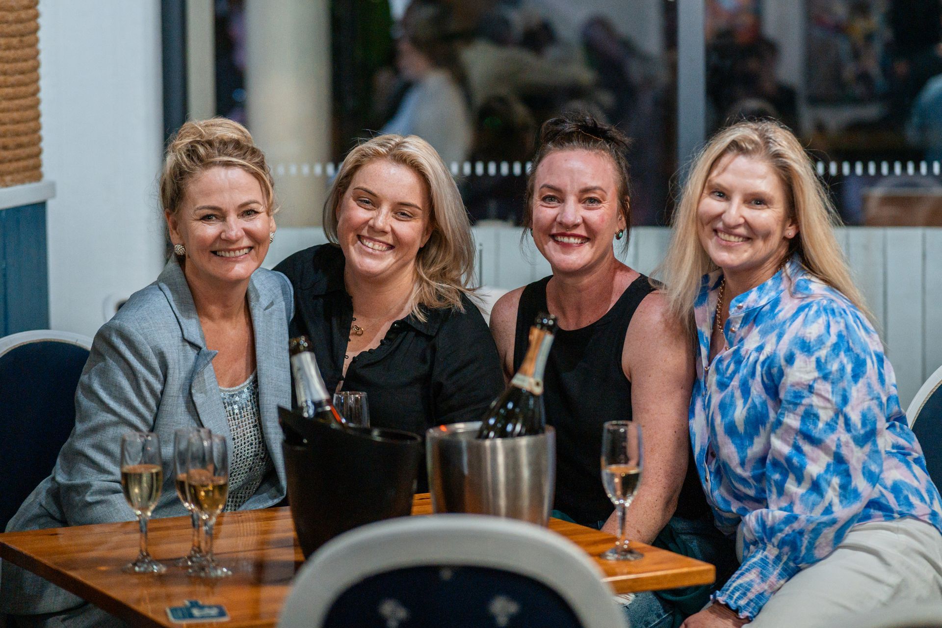A Group of Women Are Sitting at A Table with Wine Glasses and Bottles of Champagne — Chop 'n Chill in Port Macquarie, NSW