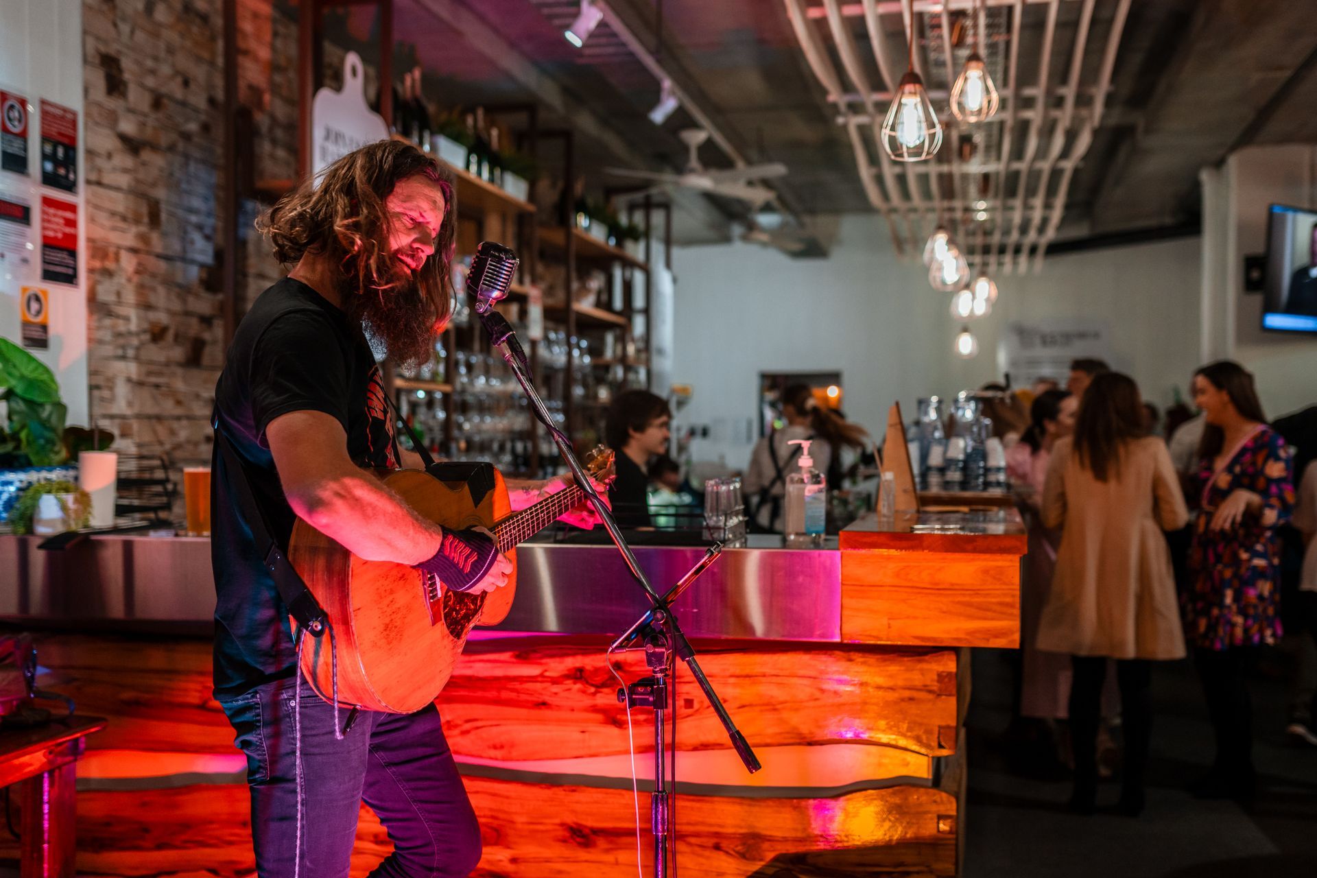 A Man Is Playing a Guitar and Singing Into a Microphone in A Bar — Chop 'n Chill in Port Macquarie, NSW