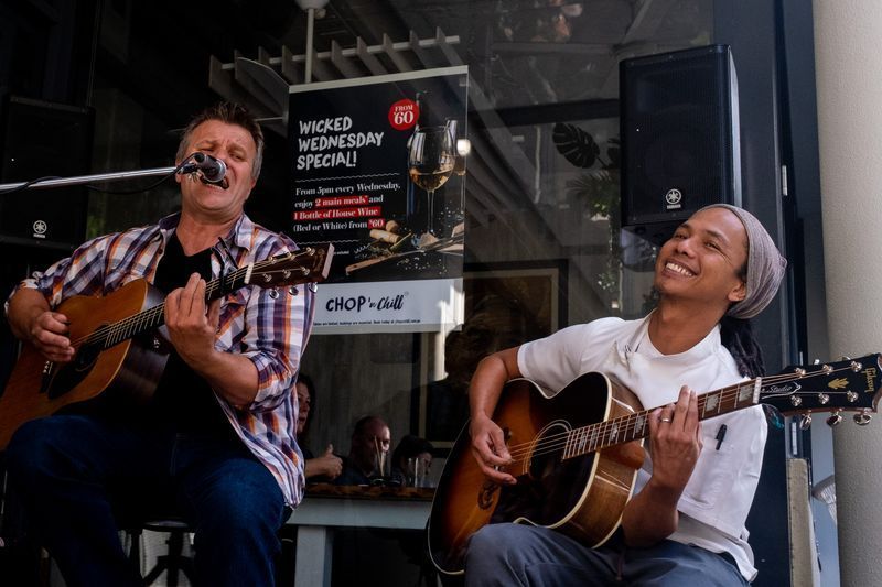Two Men Are Singing and Playing Guitars in Front of A Sign that Says Wednesday Specials — Chop 'n Chill in Port Macquarie, NSW