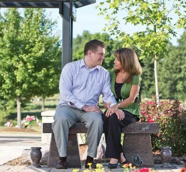 Couple sitting close on a stone bench in a sunny park, looking at each other warmly