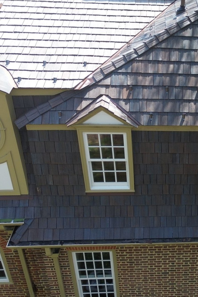 Close-up of a house roof with dark shingles and a white-trimmed dormer window above brick siding