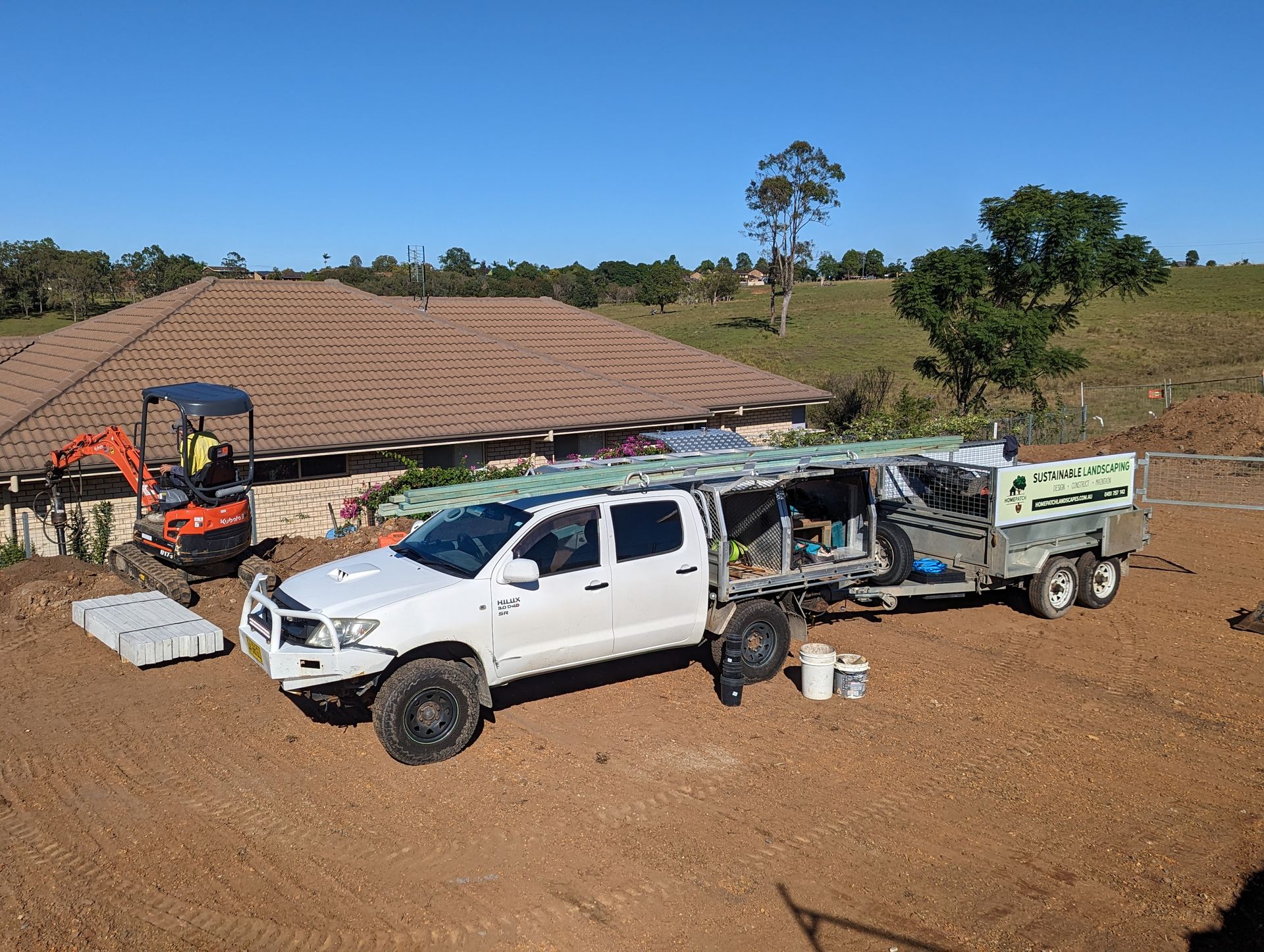 A white truck with a trailer attached to it is parked in front of a house under construction.