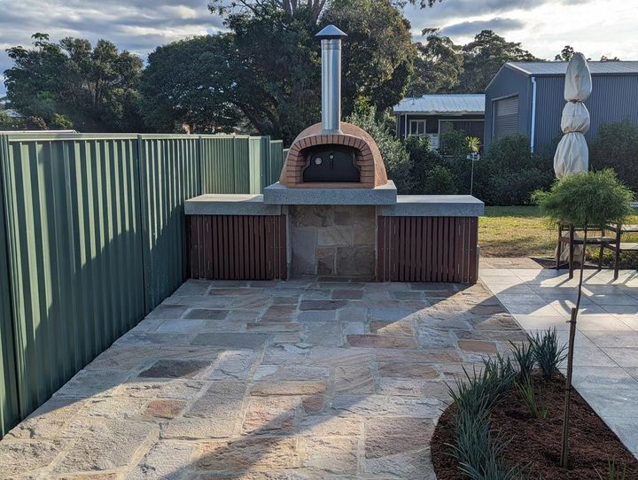 A brick oven is sitting on a patio next to a fence.