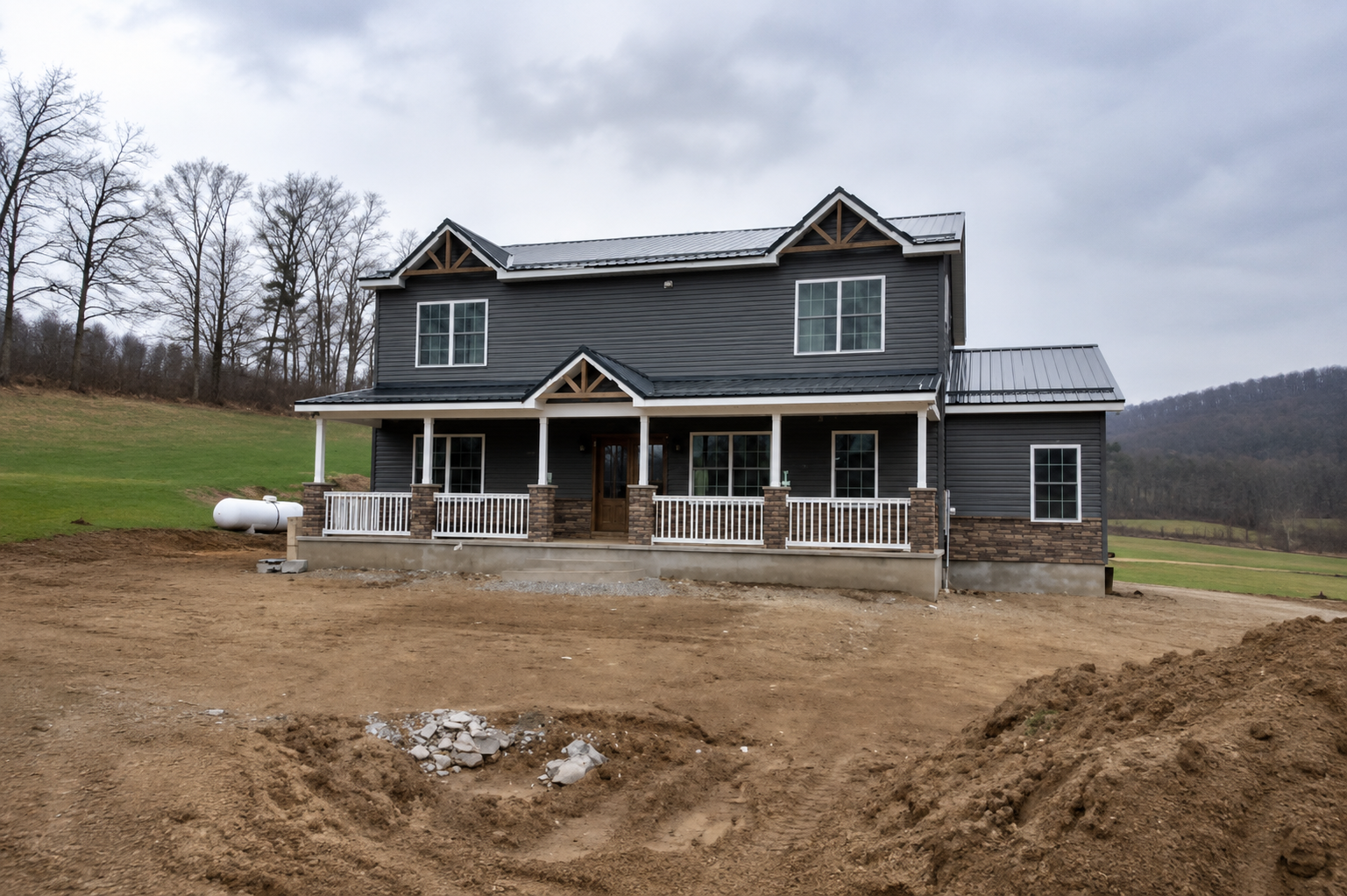Two-story gray house under construction with unfinished dirt yard and covered front porch