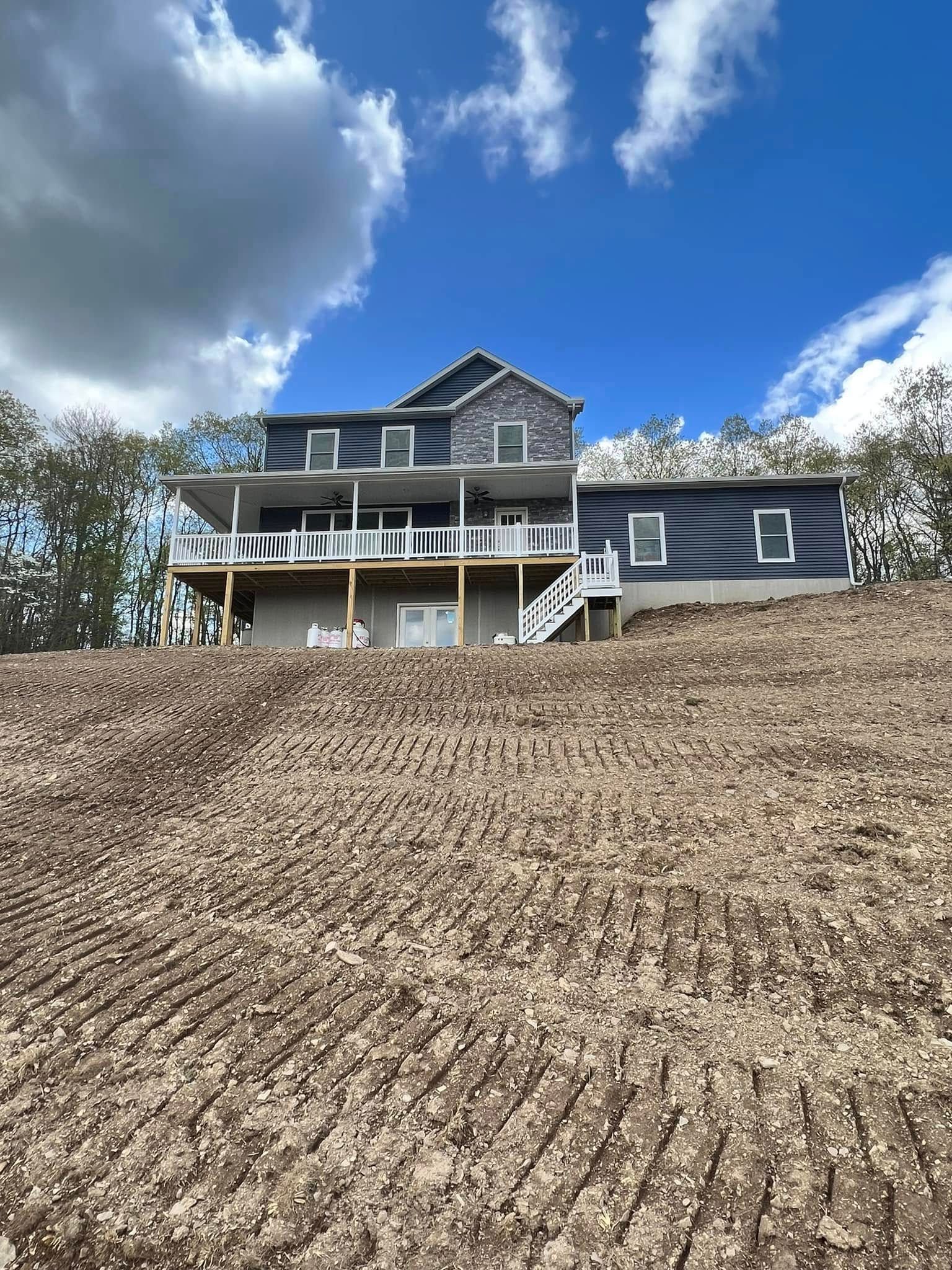 House with white porch on a wooded hillside under a blue sky with clouds