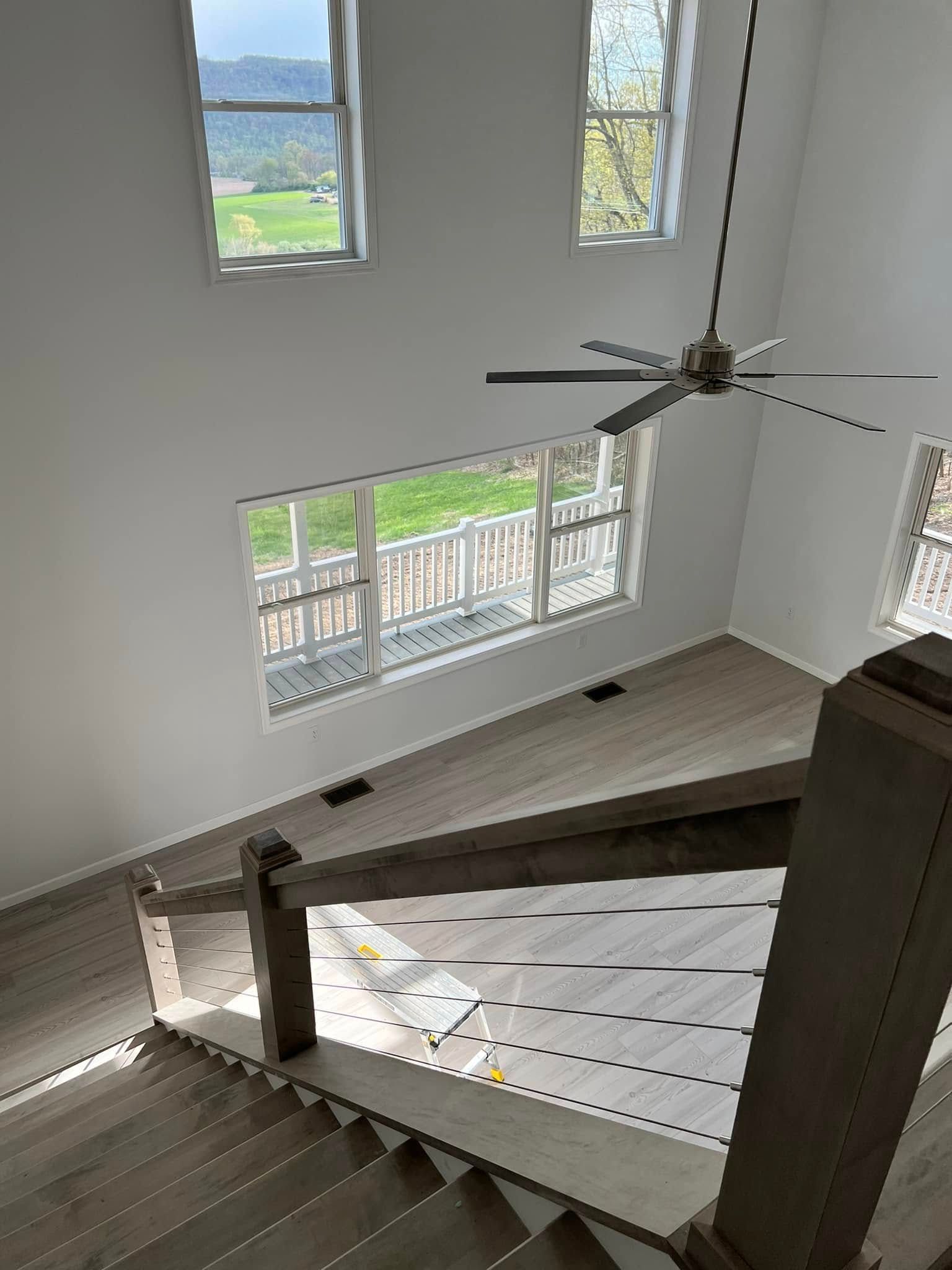 Staircase landing with white railing, large windows, and a ceiling fan in a bright foyer.