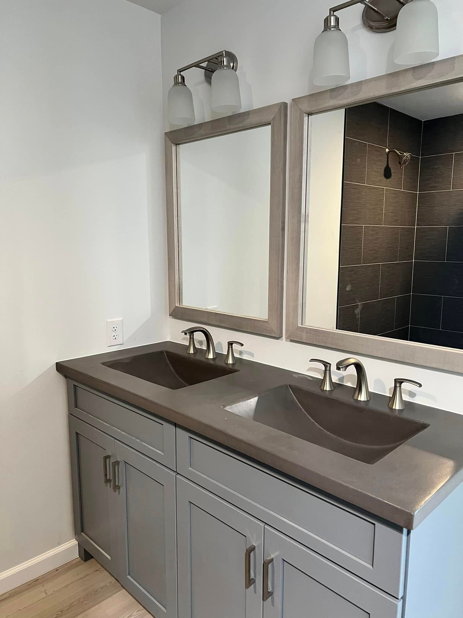 Modern double-sink bathroom vanity with dark countertop, gray cabinets, and wall mirrors above.