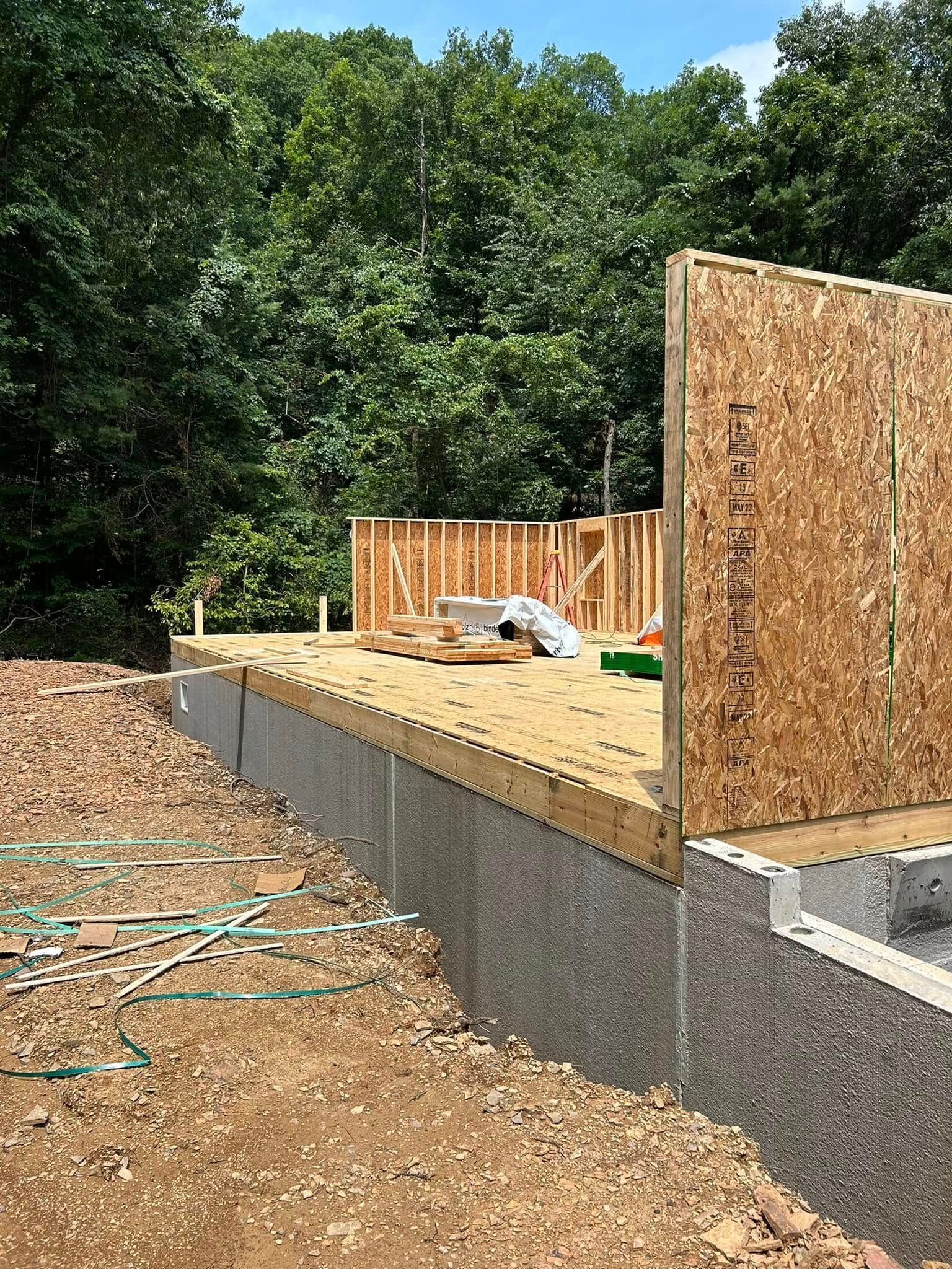 Partially built wooden house on a raised concrete foundation at a wooded construction site