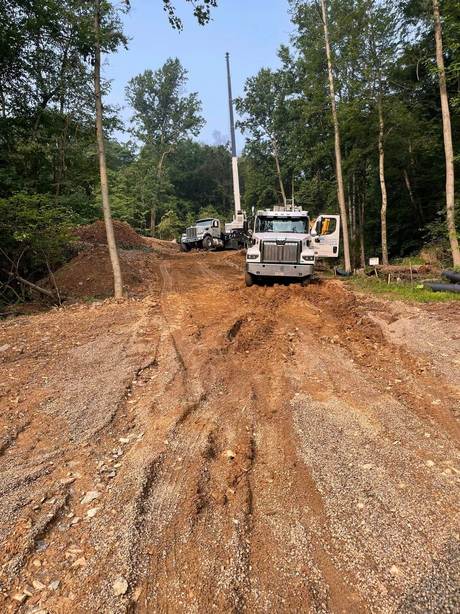 Mud-covered road with two white utility trucks in a wooded area after heavy use.