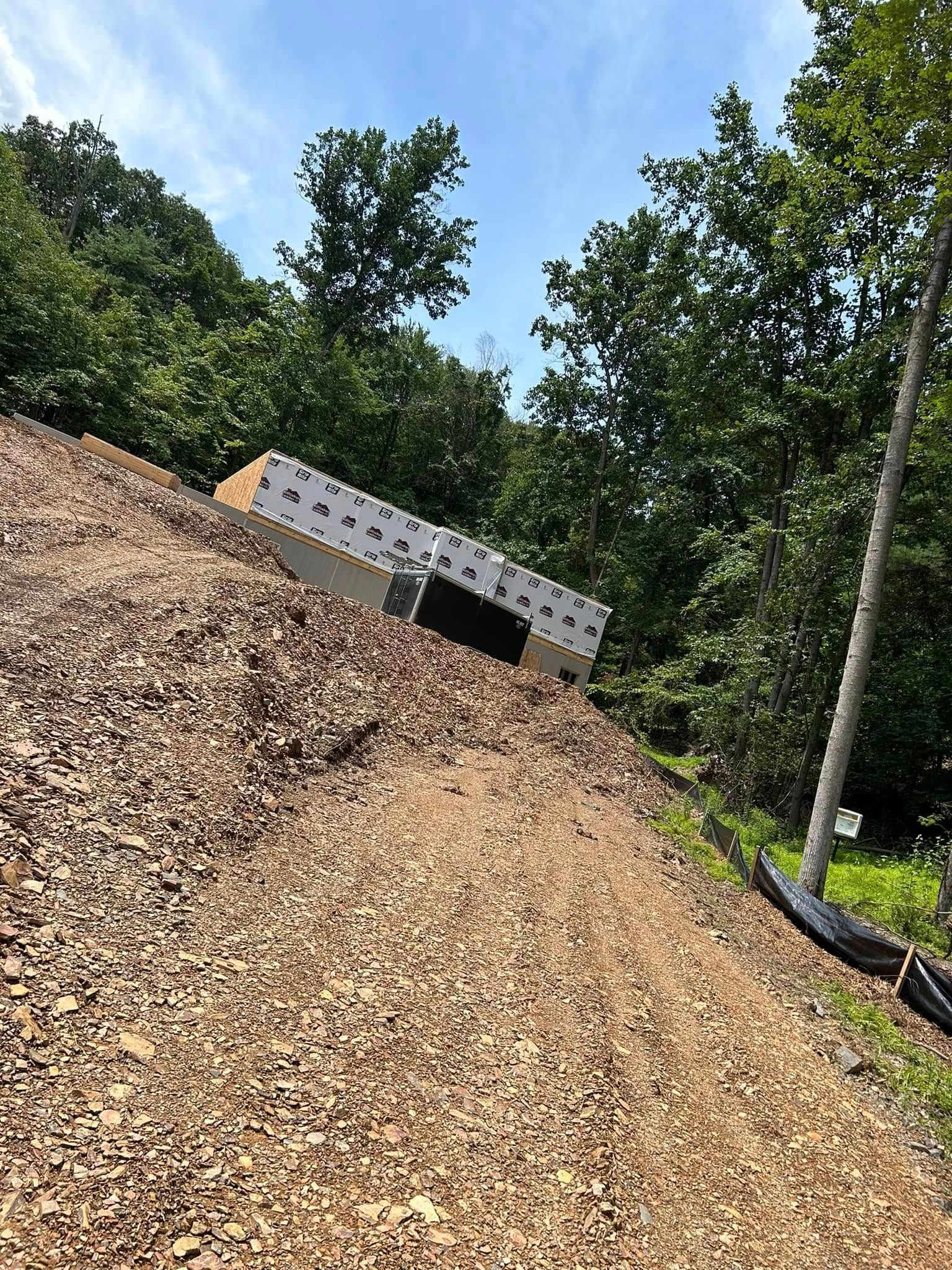 Wood chip mound at a wooded outdoor site with a white trailer partly buried beside it.
