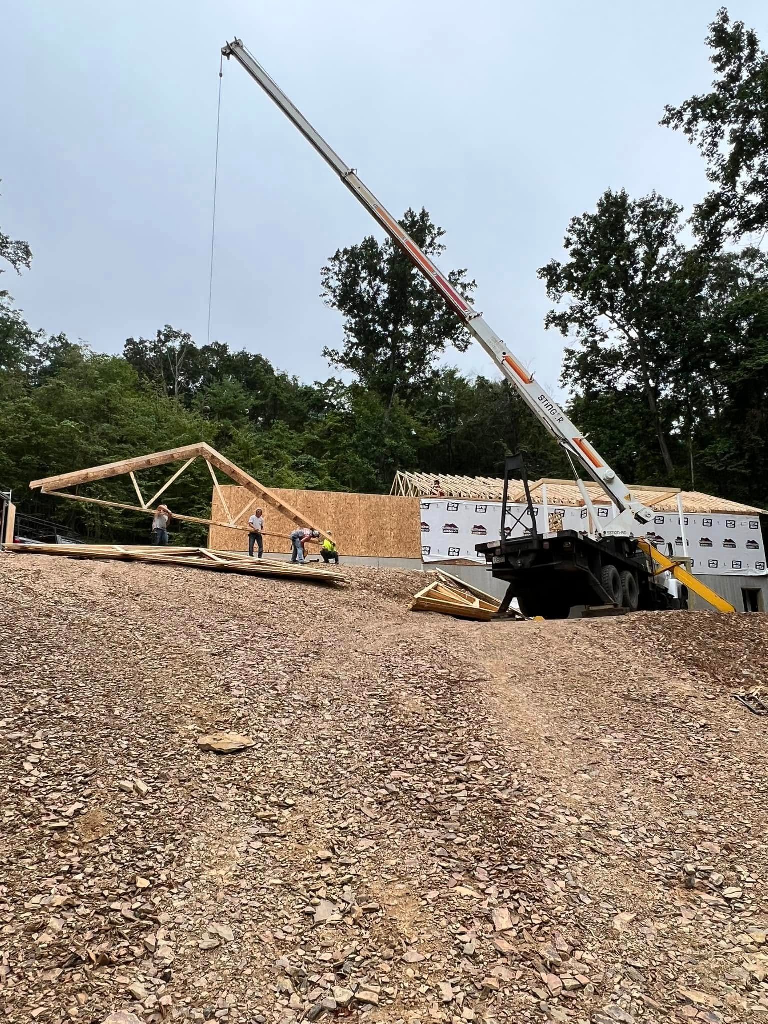 Construction site with crane, gravel pile, and partially built wooden structure under a clear sky