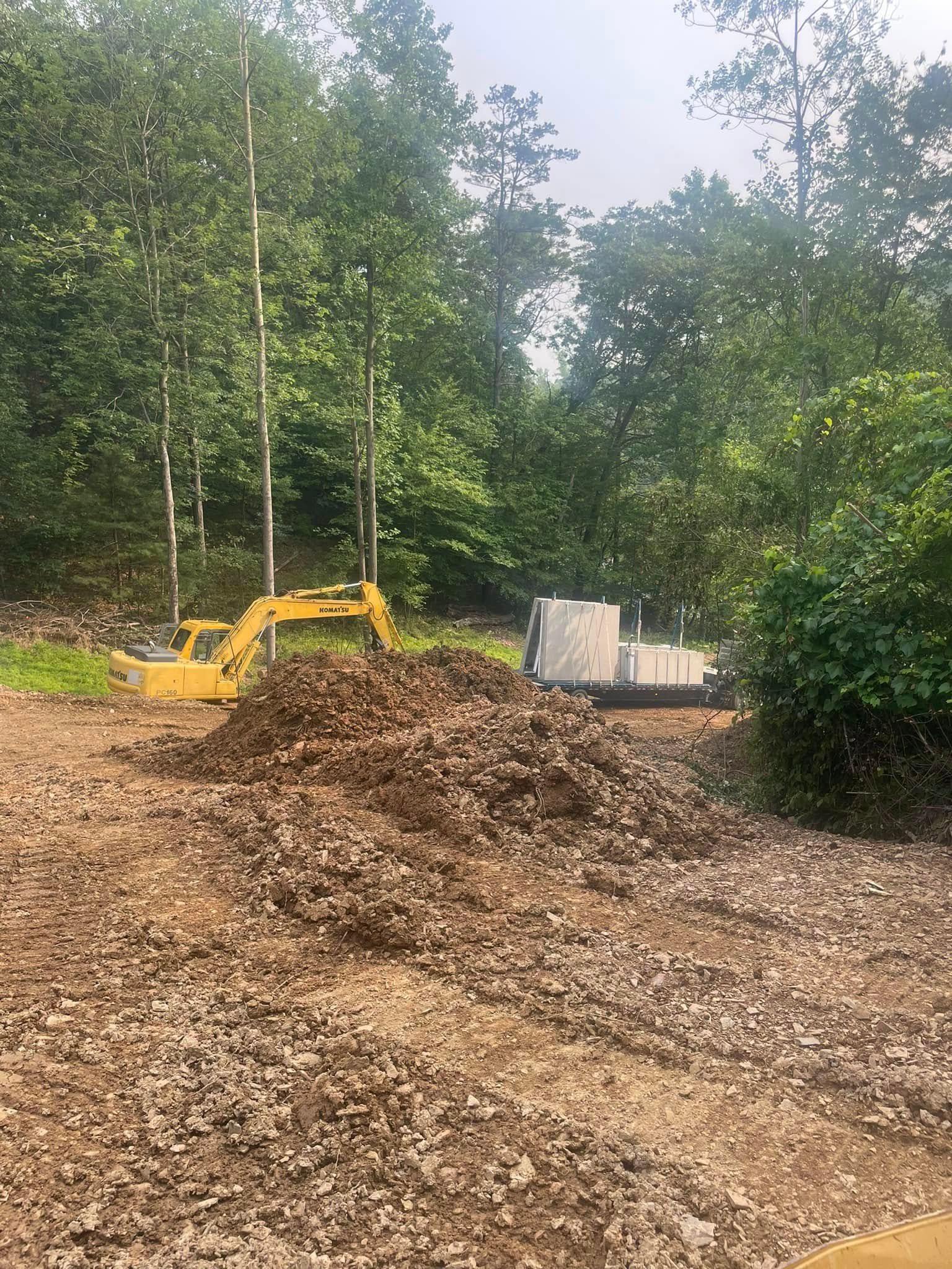 Yellow excavator beside a wood chip pile in a wooded clearing